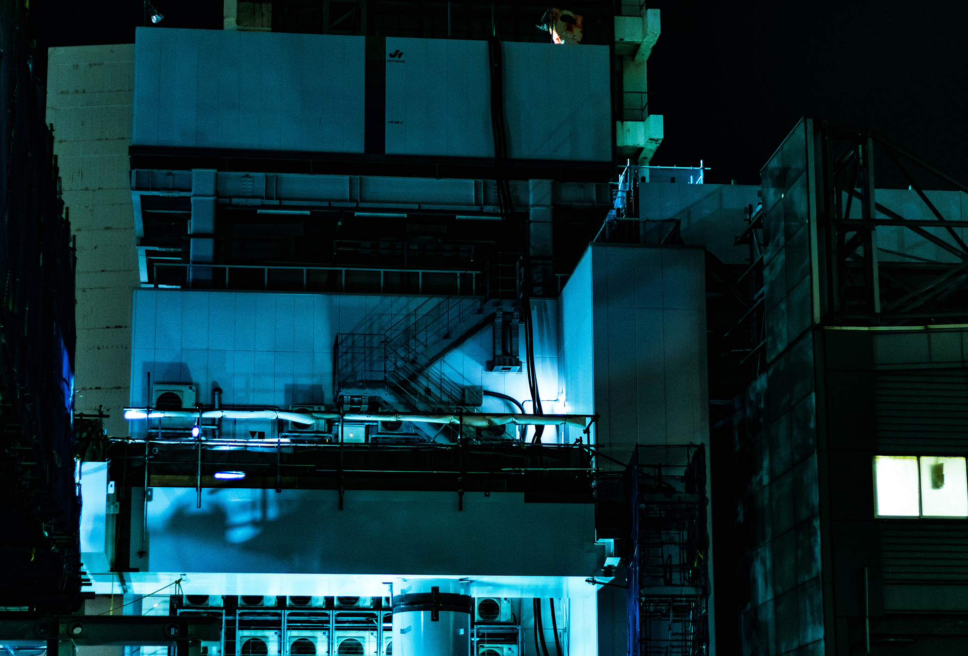 Dimly lit side of a modern building rooftop with air conditioning units and pipes on its facade.